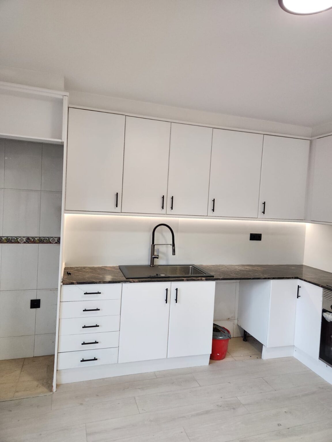 Cocina reformada con muebles blancos, iluminación LED y encimera oscura en Barcelona