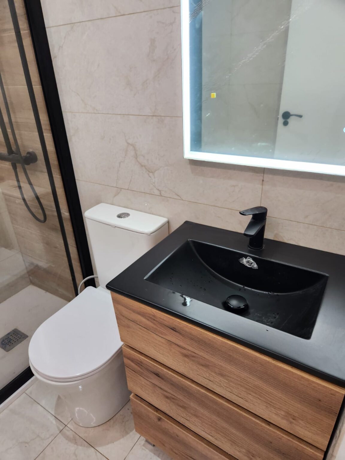 Lavabo negro sobre mueble de madera en baño reformado en vivienda de Barcelona