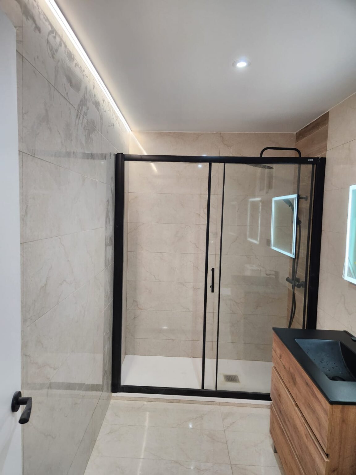 Baño reformado con ducha de cristal y mampara negra en vivienda de Barcelona