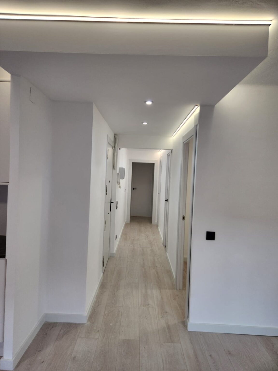 Pasillo largo con iluminación LED y suelo laminado tras reforma integral de piso en Barcelona