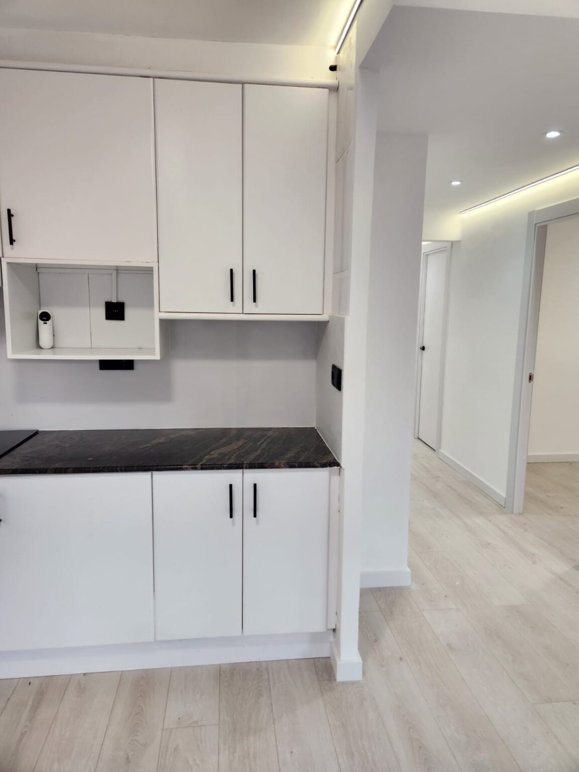 Cocina moderna con muebles blancos y encimera oscura tras reforma en vivienda de Barcelona