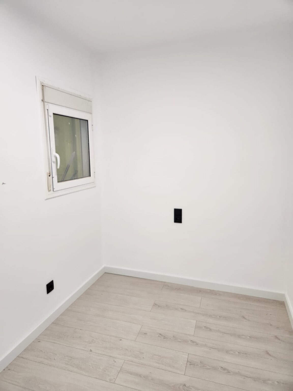 Habitación reformada con suelo laminado y paredes blancas en piso de Barcelona