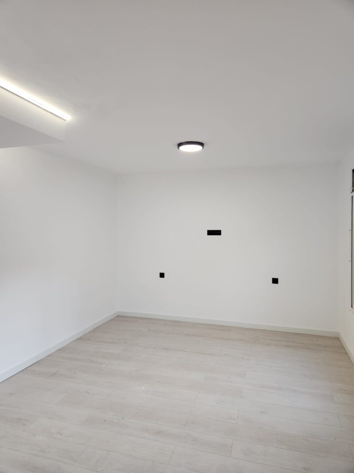 Espacio de salón reformado con iluminación moderna y suelo laminado en vivienda de Barcelona