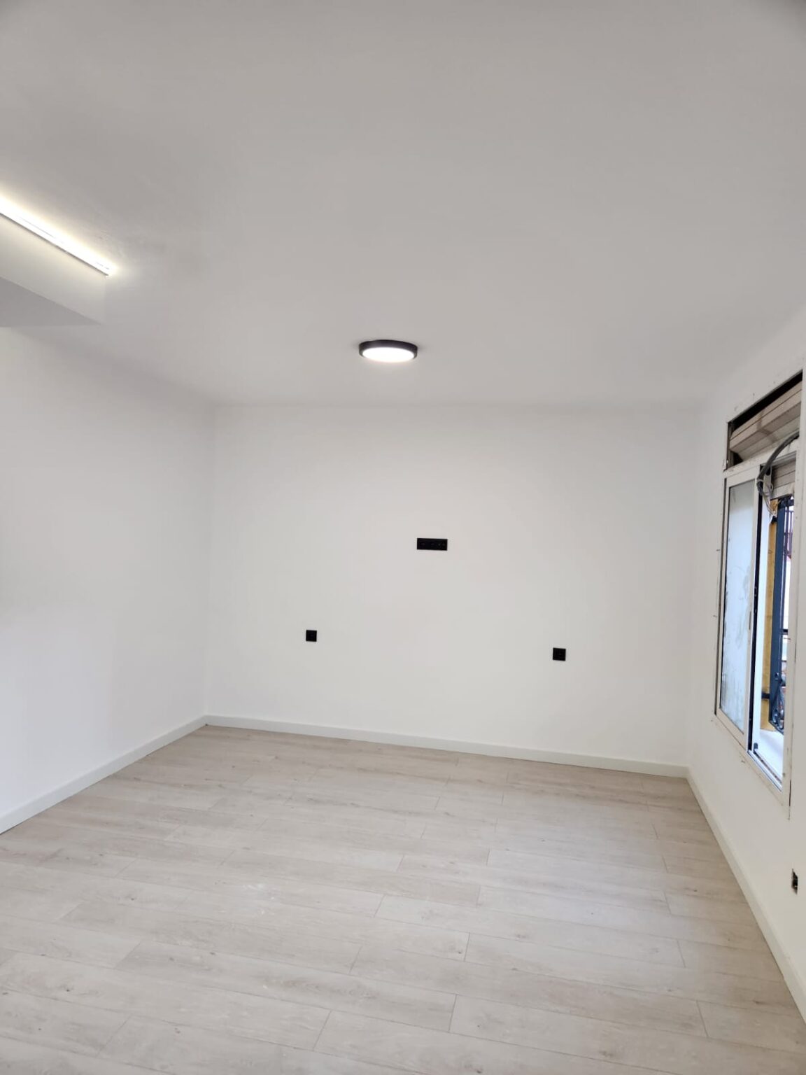 Habitación reformada con suelo laminado y paredes blancas en piso de Barcelona