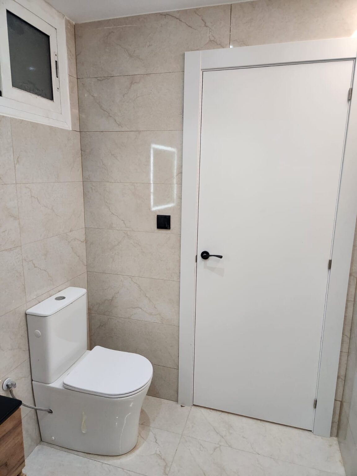 Baño reformado con inodoro suspendido, espejo iluminado y puerta blanca en vivienda de Barcelona