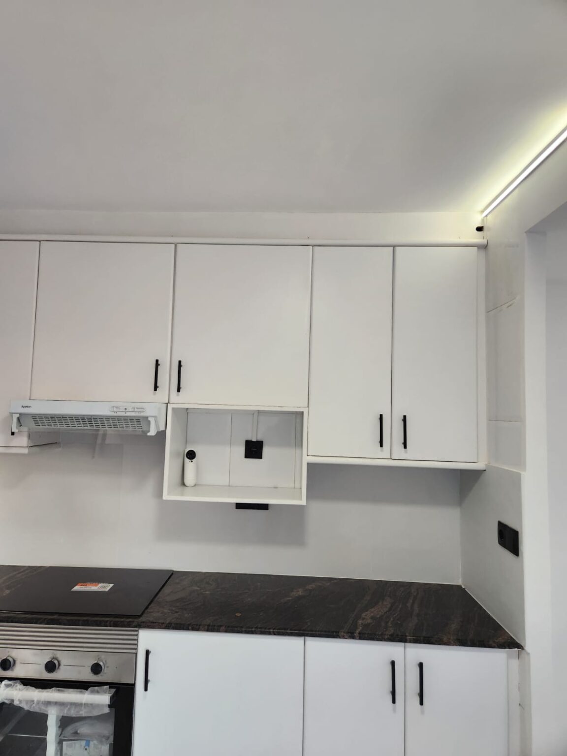 Cocina moderna reformada con muebles blancos y encimera oscura en Barcelona