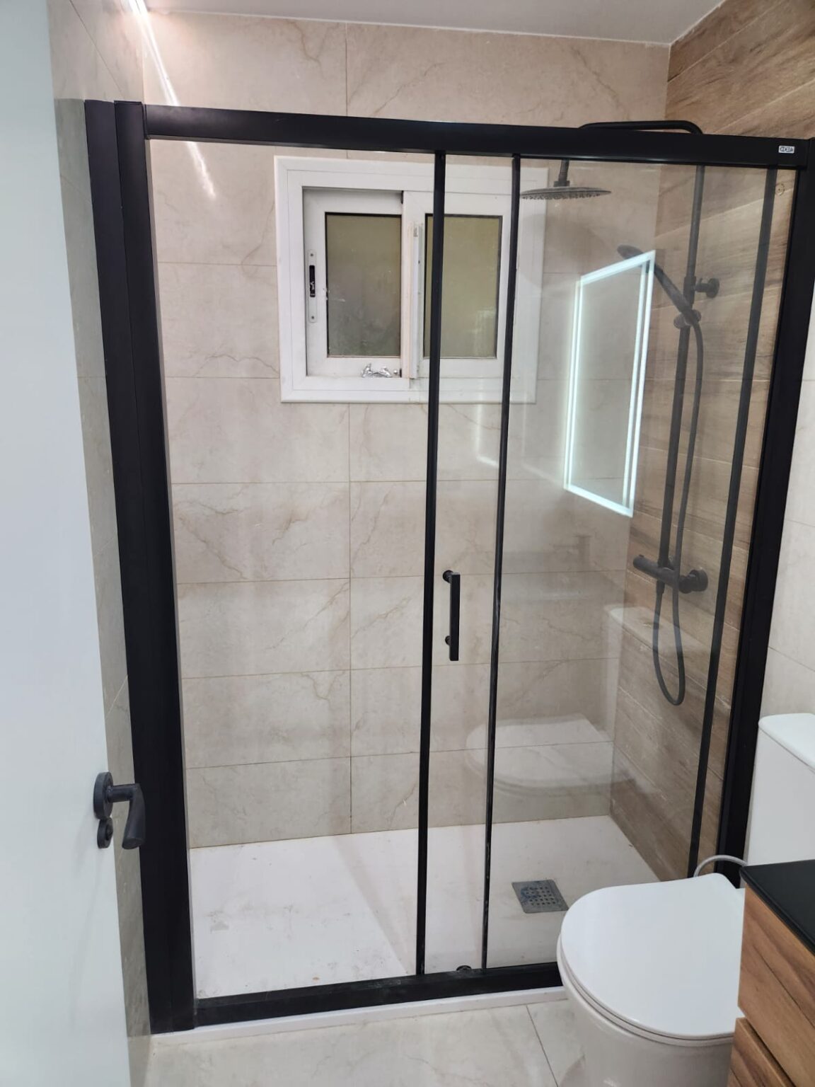 Ducha con mampara negra y azulejo moderno en baño reformado en Barcelona