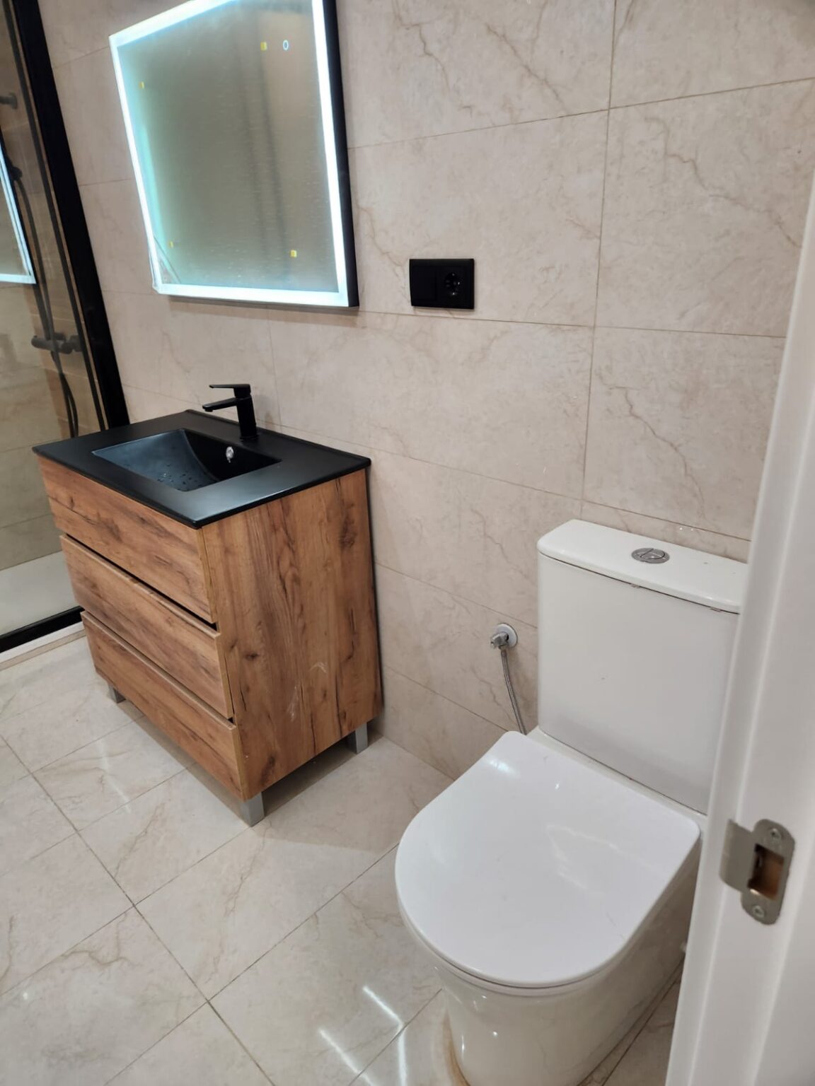 Baño reformado con mueble de madera y lavabo moderno en vivienda de Barcelona por Greyscos